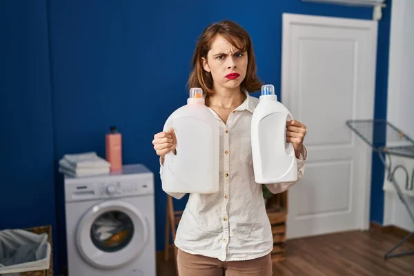 Young Beautiful Woman Holding Detergent Bottles Skeptic Nervous Frowning Upset — стоковое фото