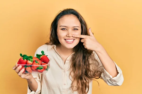 Young Hispanic Girl Holding Strawberries Pointing Hand Finger Face Nose — Stock fotografie