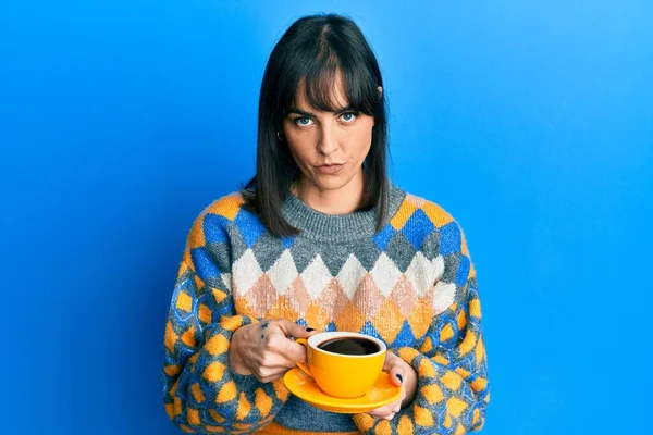Latin kökenli genç bir kadın bir fincan kahve içiyor şüpheci ve gergin, sorun yüzünden surat asıyor. negatif kişi. 