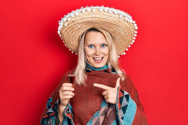 美しいですCaucasianブロンド女性身に着けているお祝いメキシコのポンチョ飲料Tequilaショット笑顔幸せなポインティングとともに手と指 — ストック写真