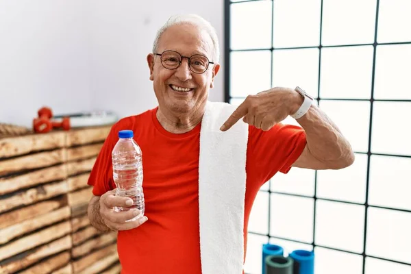 Senior man wearing sportswear and towel at the gym looking confident with smile on face, pointing oneself with fingers proud and happy.