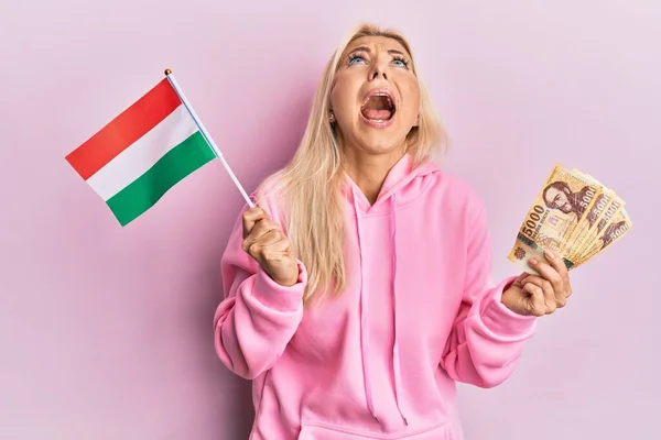 Young Blonde Woman Holding Hungary Flag Forint Banknotes Angry Mad — Stock fotografie
