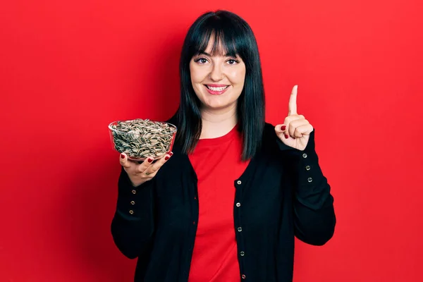 Young Hispanic Woman Holding Sunflower Seeds Bowl Smiling Idea Question — Stok fotoğraf