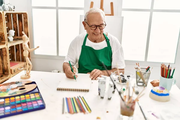 高级灰白头发的画家坐在艺术工作室的桌子上 开心地微笑着绘画 — 图库照片