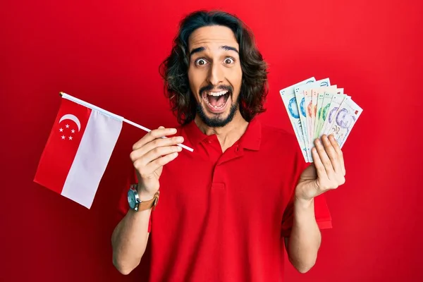 Joven Hombre Hispano Sosteniendo Bandera Singapur Dólares Celebrando Loco Sorprendido —  Fotos de Stock