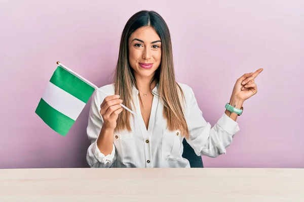 Young Hispanic Woman Holding Nigeria Flag Sitting Table Smiling Happy — Fotografia de Stock