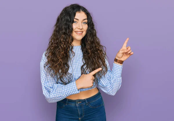 Gündelik kıyafetler giyen, gülümseyen ve kameraya bakan genç İspanyol kız iki eliyle ve parmaklarıyla kenarı işaret ediyor.. 