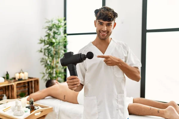 Young Hispanic Man Holding Therapy Massage Gun Wellness Center Smiling —  Fotos de Stock