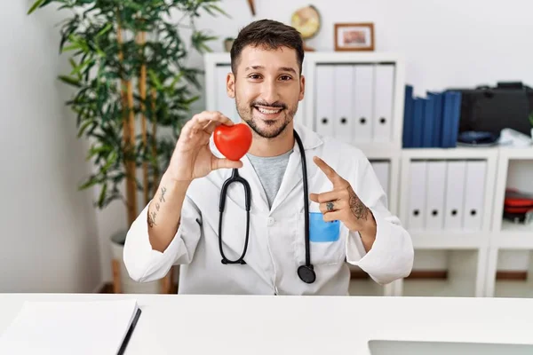 Young Doctor Holding Heart Medical Clinic Smiling Happy Pointing Hand — Zdjęcie stockowe