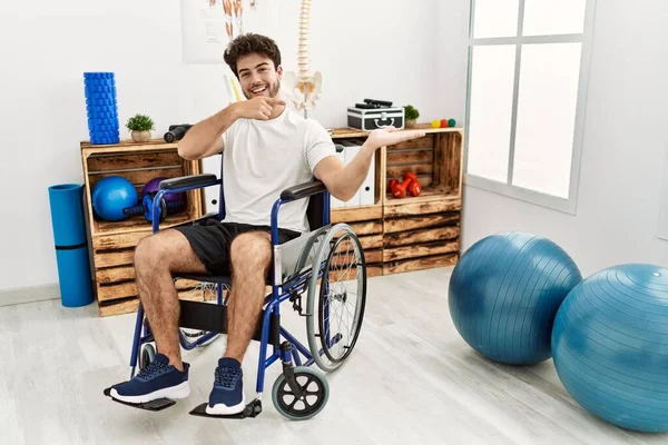 Hispanic Man Sitting Wheelchair Physiotherapy Clinic Amazed Smiling Camera While — Stok fotoğraf