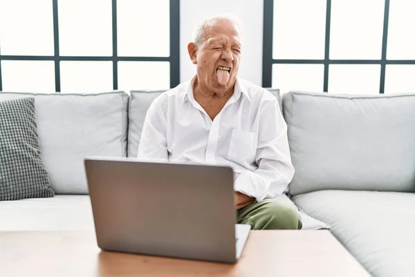 Senior Man Using Laptop Home Sitting Sofa Sticking Tongue Out — Foto de Stock