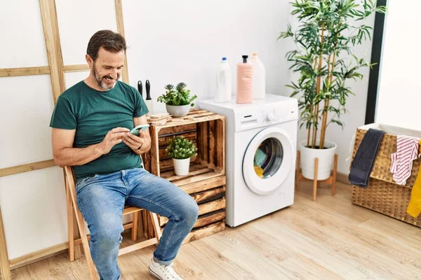 Middle Age Hispanic Man Doing Laundry Using Smartphone Waiting Home — Fotografia de Stock