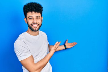 Sakallı, beyaz tişörtlü genç bir Arap adam gülümseyerek içeri girmeye davet ediyor. 