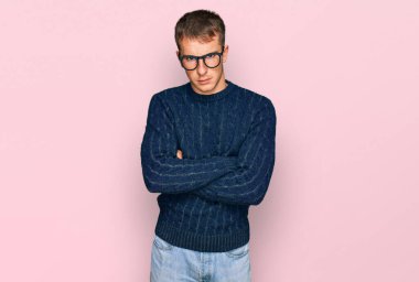 Young blond man wearing casual clothes and glasses skeptic and nervous, disapproving expression on face with crossed arms. negative person. 