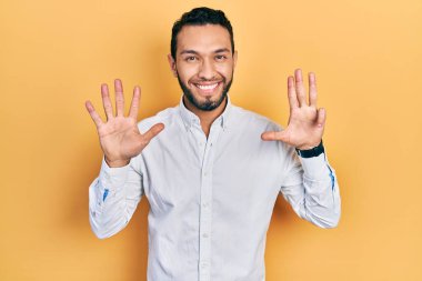 Hispanic man with beard wearing business shirt showing and pointing up with fingers number nine while smiling confident and happy. 