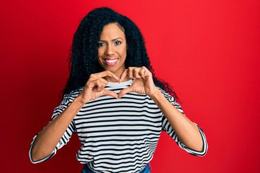 Orta yaşlı Afro-Amerikalı kadın, sıradan kıyafetler giyip, aşık gülümsüyor, elleriyle kalp sembolü yapıyor. romantik kavram. 