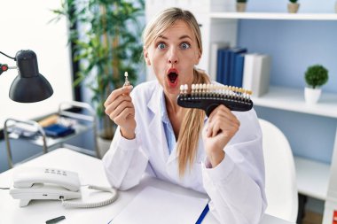 Beautiful dentist woman comparing teeth whitening afraid and shocked with surprise and amazed expression, fear and excited face. 