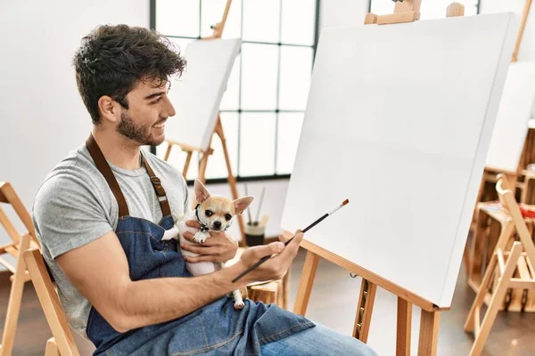 Młody Latynos Artysta Człowiek Uśmiecha Szczęśliwy Trzymając Psa Malarstwo Studio — Zdjęcie stockowe