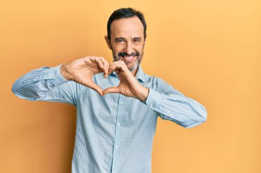 Orta yaşlı İspanyol bir adam, gündelik giysiler giymiş, aşkta gülümseyen, elleriyle kalp sembolü yapan. romantik kavram. 