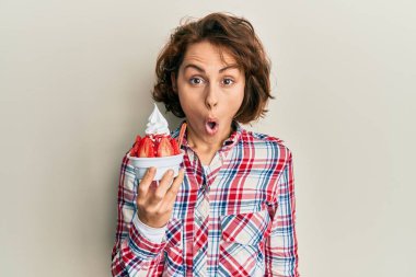 Genç esmer kadın çilekli dondurma yiyor korkmuş ve ağzı açık şaşkınlıkla şaşırmış, inançsız yüz. 