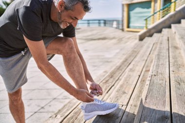 Orta yaşlı İspanyol bir adam gülümsüyor. Kendine güveni tam, ayakkabısını bağlıyor.
