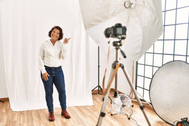 Orta yaşlı İspanyol bir kadın fotoğraf stüdyosunda mankenlik yapıyor. Gülümsüyor, mutlu bir şekilde işaret ediyor. 
