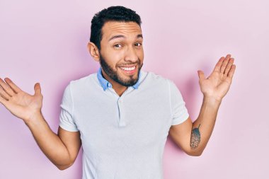 Hispanic man with beard wearing casual white t shirt clueless and confused with open arms, no idea and doubtful face. 