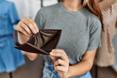 Young caucasian customer woman with unhappy expression showing empty purse at clothing store.