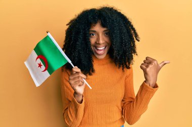 Afro saçlı, Cezayir bayrağı tutan Afro-Amerikalı bir kadın başparmağını kaldırıyor ve ağzı açık gülümsüyor. 