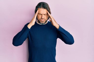 Orta yaşlı, yakışıklı, sıradan kıyafetler giyen, elleri kafasında, stresten baş ağrısı çeken bir adam. migren ağrısı. 