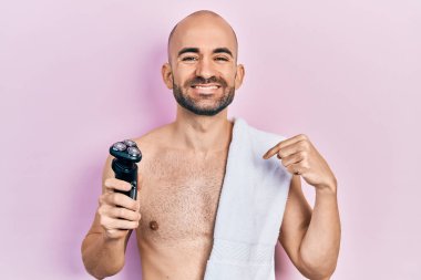 Genç kel adam elinde jiletle mutlu ve gururlu bir gülümsemeyi işaret ediyor. 