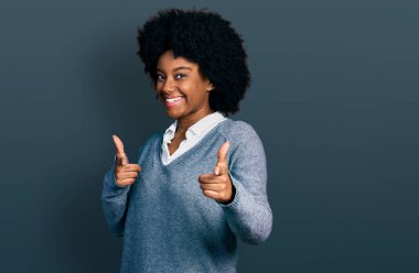 İş kıyafetleri giymiş genç Afro-Amerikalı kadın mutlu ve komik yüzüyle kamerayı işaret ediyor. iyi enerji ve titreşimler. 