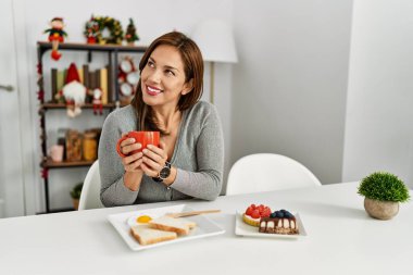 Genç Latin kadın kahvaltısını evde Noel dekoru başında yapıyor.