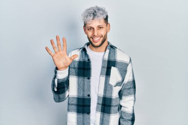 Young hispanic man with modern dyed hair wearing casual shirt showing and pointing up with fingers number five while smiling confident and happy. 