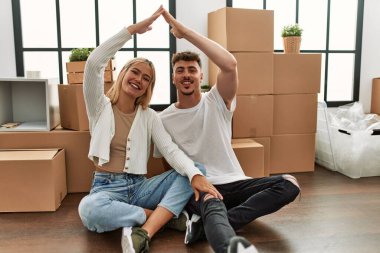 Genç beyaz çift gülümseyerek yeni evlerinde ev sembolü yapıyor..