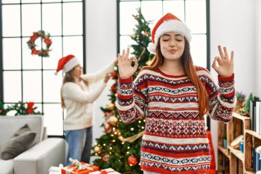 Evde güzel bir çift Noel ağacının yanında durup rahatlıyor ve parmaklarıyla meditasyon yaparken gözleri kapalı gülümsüyor. yoga konsepti. 