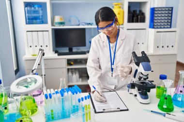 Laboratuvarda çalışan, bilim adamı üniforması giyen genç Latin kadın.