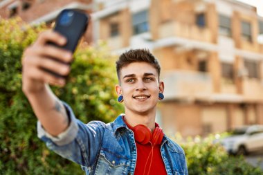 Genç beyaz adam gülümsüyor ve şehirde selfie çekiyor.