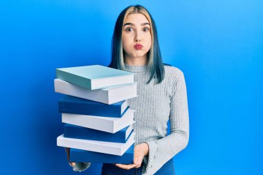 Genç, modern bir kız elinde bir yığın kitap tutarak komik suratıyla yanaklarını şişiriyor. Ağzı havayla şişer, havayı yakalar.. 