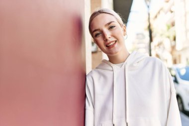 Modern beyaz saç stili ile genç ve güzel bir kadın mutlu bir şekilde dışarıda duvara yaslanıyor.