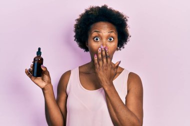 Yüzünde yüz serumu olan, ağzı elle kaplayan, şok olmuş ve hata yapmaktan korkan genç bir Afro-Amerikalı kadın. şaşırmış ifade 