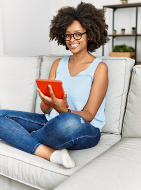 Genç Afro-Amerikalı kadın evde dokunmatik ped kullanarak gülümsüyor.