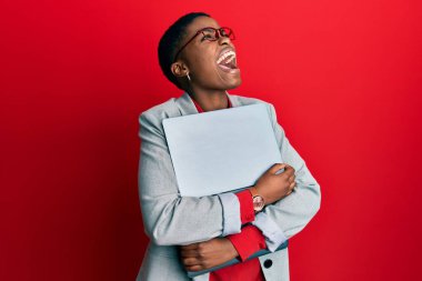 Young african american businesswoman holding laptop angry and mad screaming frustrated and furious, shouting with anger looking up. 