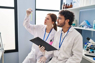 Erkek ve kadın bilim adamı partnerler laboratuarda elinde pano olan test tüpü arıyorlar.