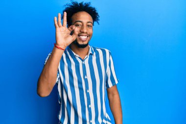 Young african american man with beard wearing casual striped shirt smiling positive doing ok sign with hand and fingers. successful expression. 