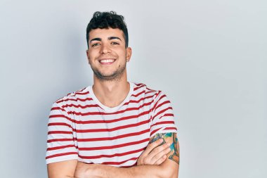 Gündelik kıyafetler giyen, kollarını kavuşturup kameraya gülümseyen genç İspanyol adam. pozitif kişi. 