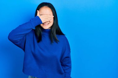 Young chinese girl wearing casual clothes smiling and laughing with hand on face covering eyes for surprise. blind concept. 