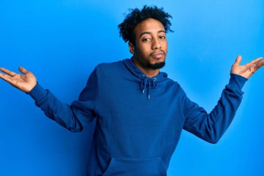 Young african american man with beard wearing casual sweatshirt clueless and confused with open arms, no idea and doubtful face. 