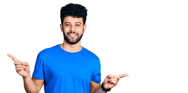 年轻的阿拉伯男子 留着胡子 穿着休闲的蓝色T恤 微笑着 自信地指指点着不同的方向 复制广告空间 — 图库照片