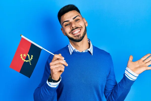 Joven Hispano Con Barba Sosteniendo Bandera Angola Celebrando Logro Con —  Fotos de Stock